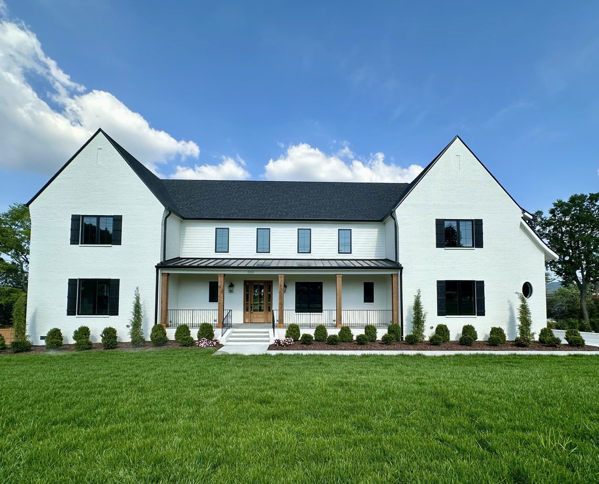 Front exterior of the white brick and siding home with a wood column porch and a green lawn at 3300 Trimble Road, one of the Green Hills homes for sale in Green Hills Nashville