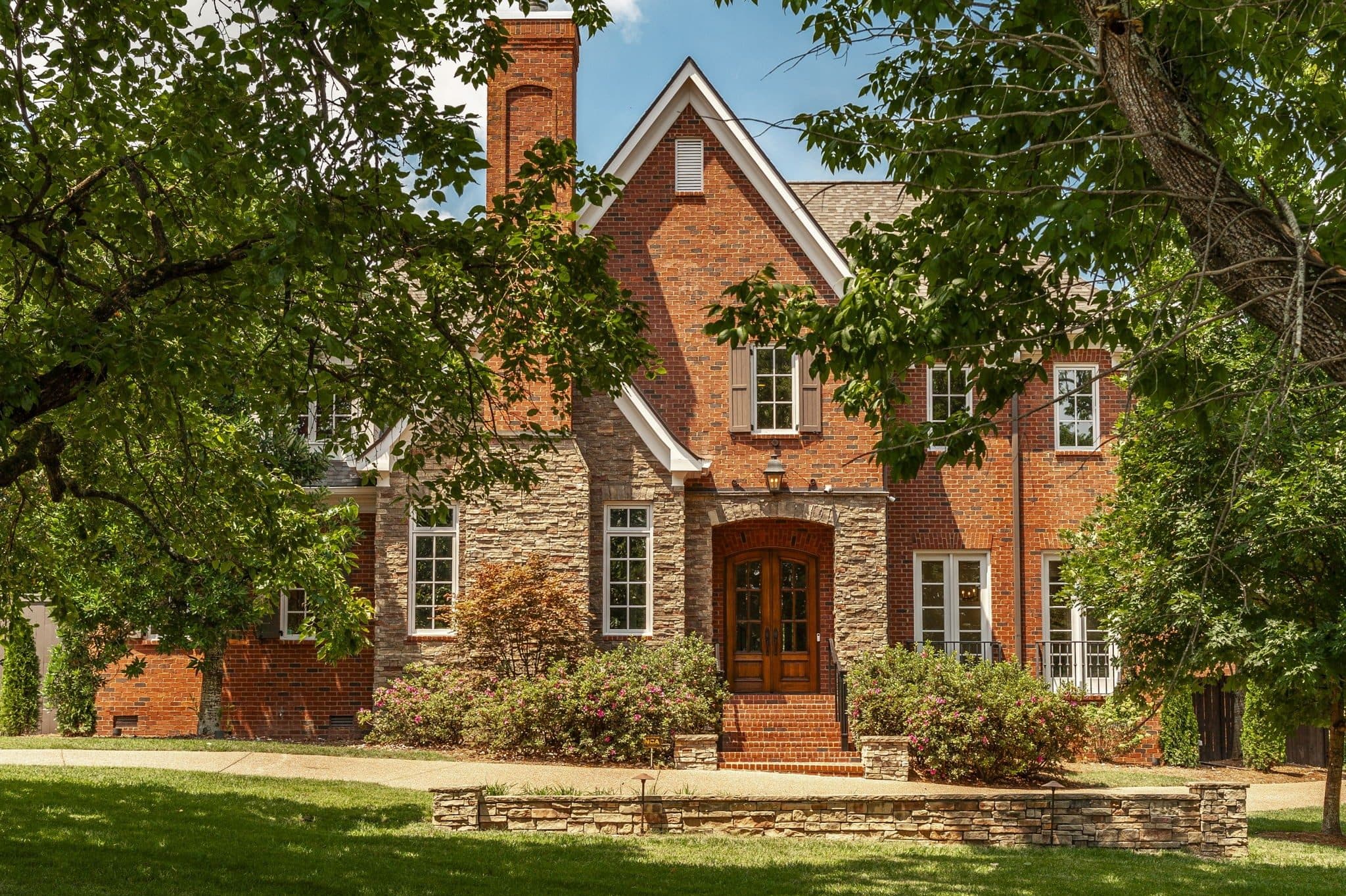 Front exterior of the brick and stone home with an arched entry and mature trees at 4301 Wallace Lane, one of the Green Hills homes for sale in Green Hills Nashville