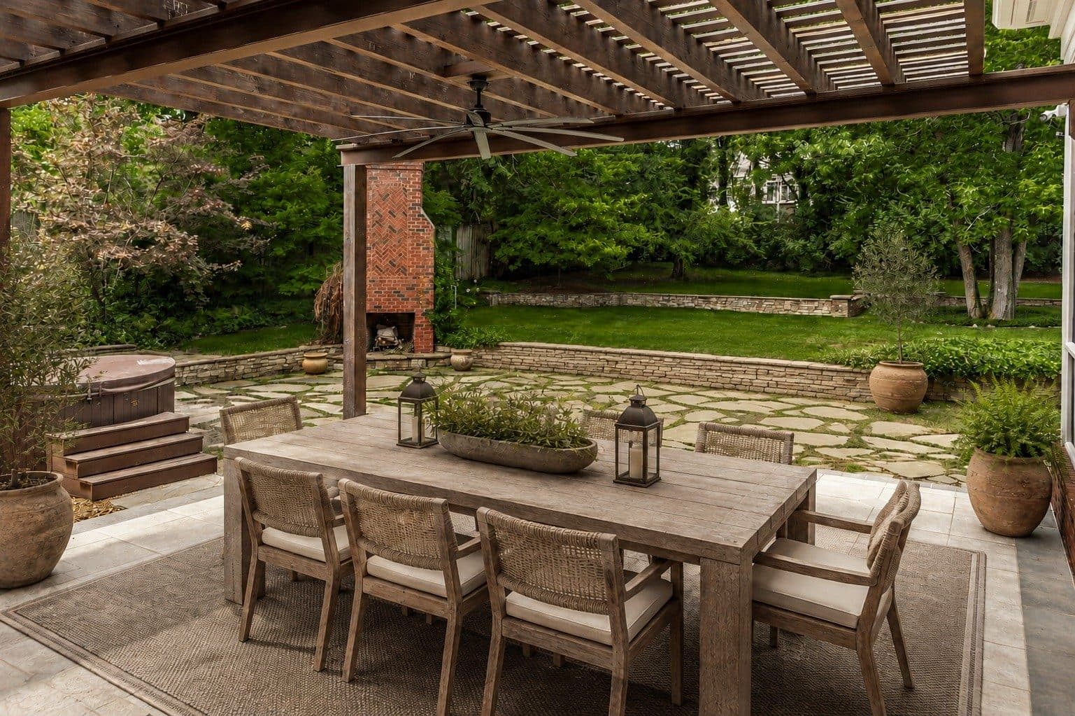 Pergola covered outdoor dining table with a hot tub and brick fireplace beyond at 4301 Wallace Lane, Green Hills Nashville