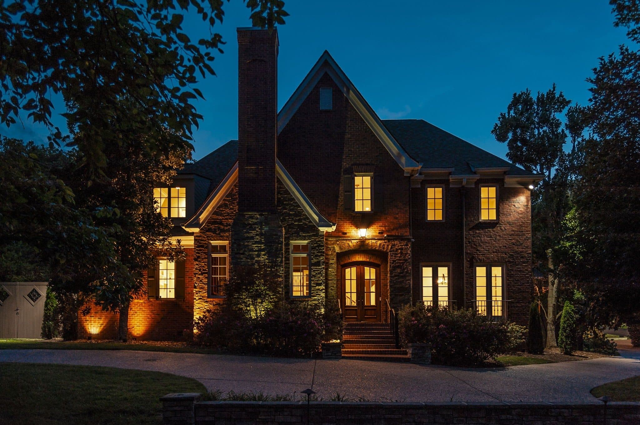 Front of the brick and stone home lit at dusk with landscape lighting at 4301 Wallace Lane, Green Hills Nashville